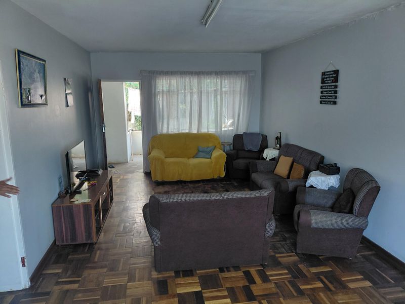 A living room featuring traditional parquet flooring and natural light through a large window, offering a functional space with potential for modern updates.