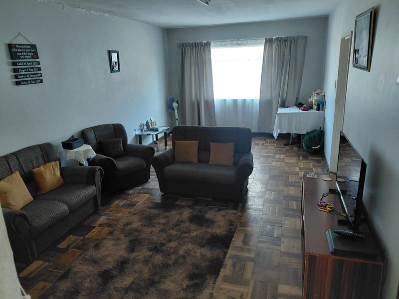 A living room featuring traditional parquet flooring and a large window, requiring some cosmetic attention to the ceiling and wall finishes.
