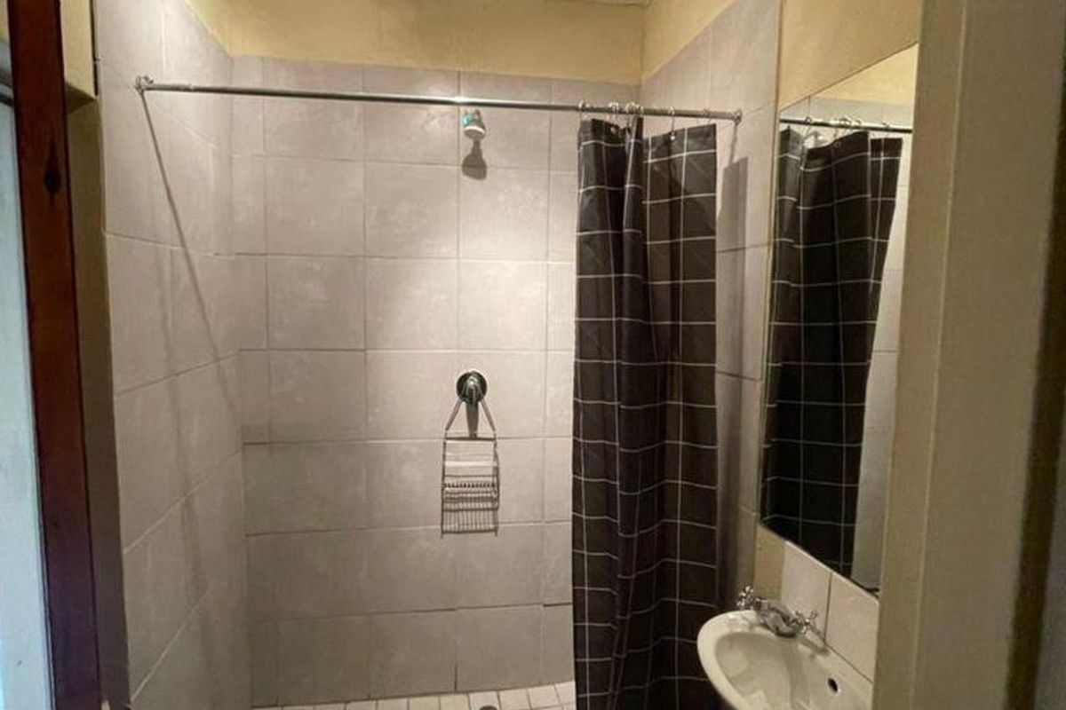Compact bathroom featuring a tiled walk-in shower, wall-mounted basin, and mirror. The space requires cosmetic updates to improve its overall condition and finish.