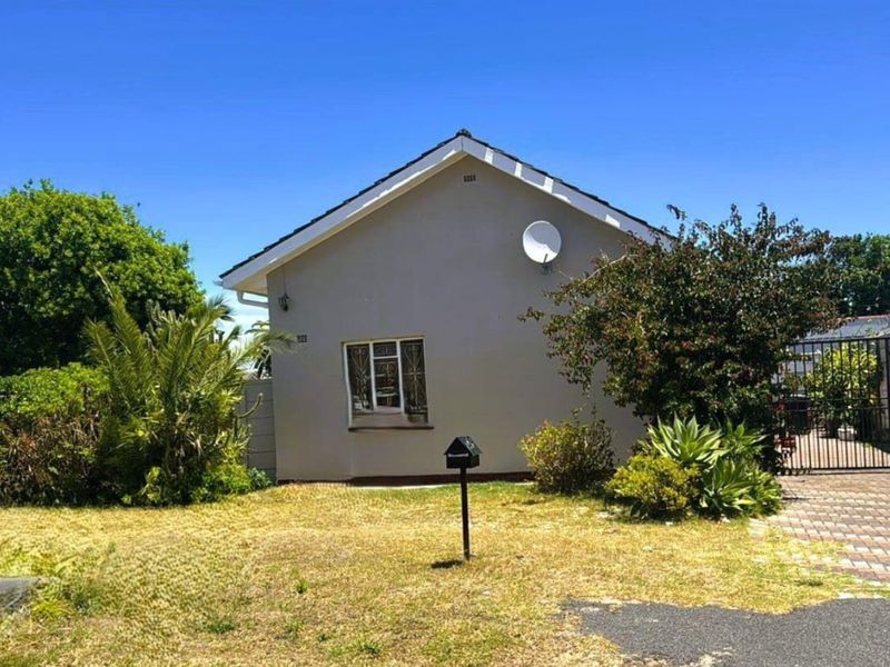 Front view of a detached house featuring a paved driveway, metal security gate, and established garden area.