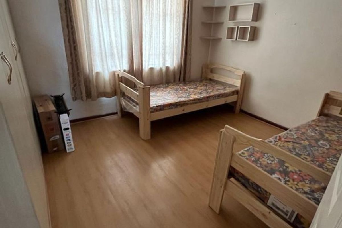 A functional bedroom featuring laminate flooring, a built-in wardrobe, and wall-mounted shelving, offering a neutral space ready for personalization.
