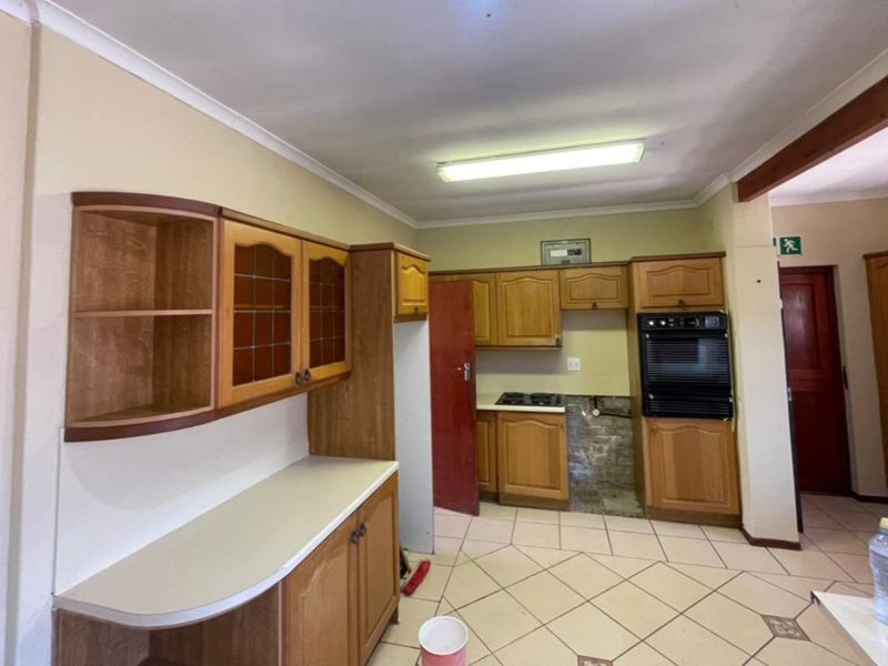 A dated kitchen featuring wooden cabinetry, built-in oven, and hob, with tiled flooring and an area requiring repair where an appliance was previously installed.