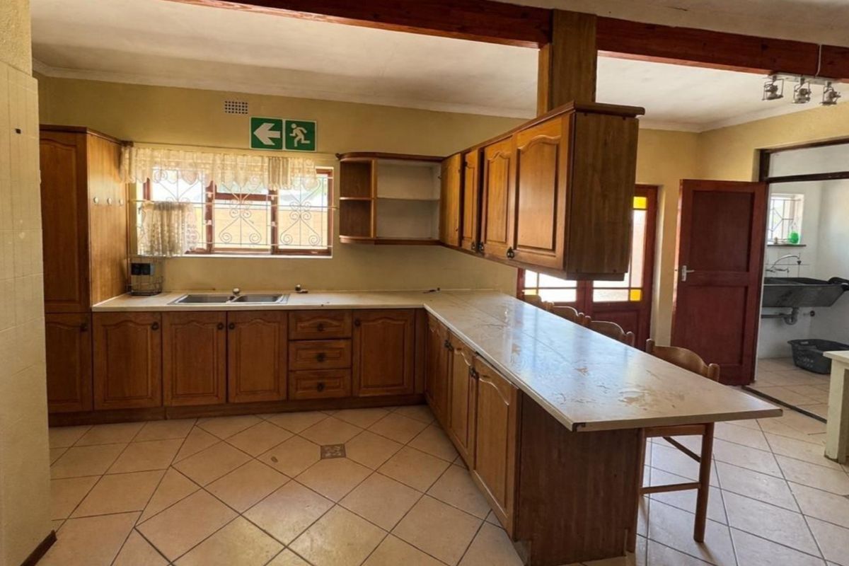 A functional kitchen featuring wooden cabinetry, laminate countertops, and ceramic floor tiles, with an open layout connecting to a secondary utility area.