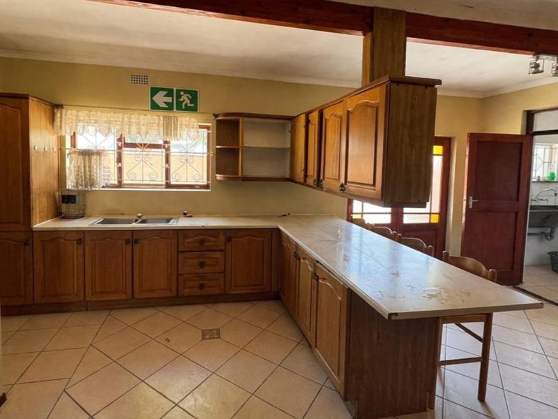 A functional kitchen featuring wooden cabinetry, laminate countertops, and ceramic floor tiles, with an open layout connecting to a secondary utility area.