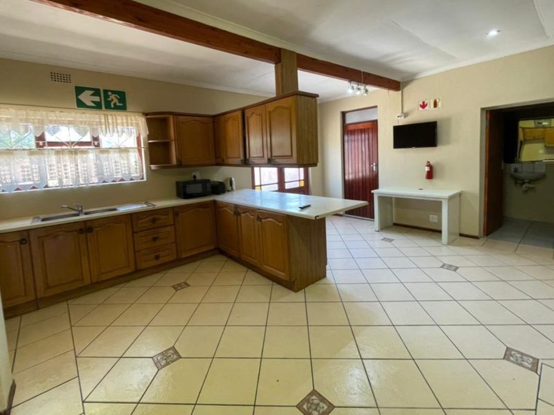 Open-plan kitchen area featuring traditional wooden cabinetry, laminate countertops, and tiled flooring, with an exposed wooden ceiling beam and direct access to adjacent rooms.