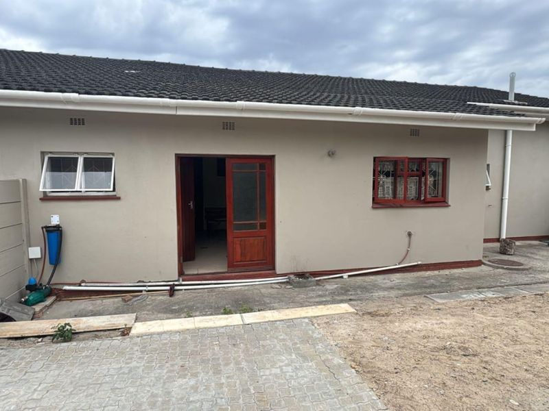 Rear exterior view of the house featuring a tiled roof, timber door, security window bars, and an external water filtration system.