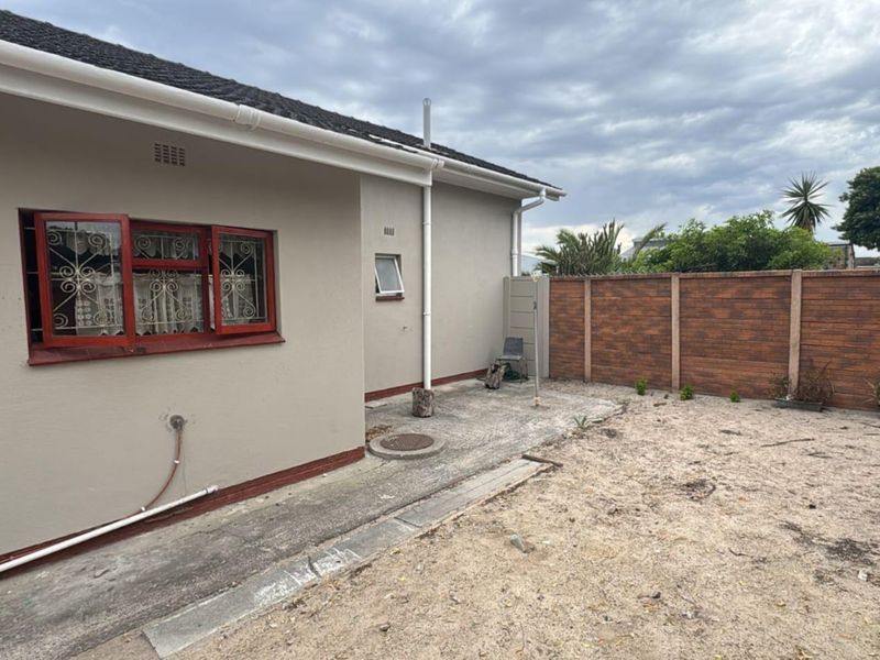Rear exterior view of the property featuring a concrete apron, brick boundary wall, and security-fitted windows.