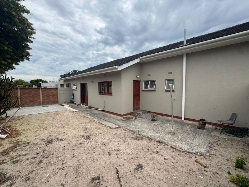 Rear view of the house featuring a concrete patio, tiled roof, and an unlandscaped sandy backyard area enclosed by a precast boundary wall.