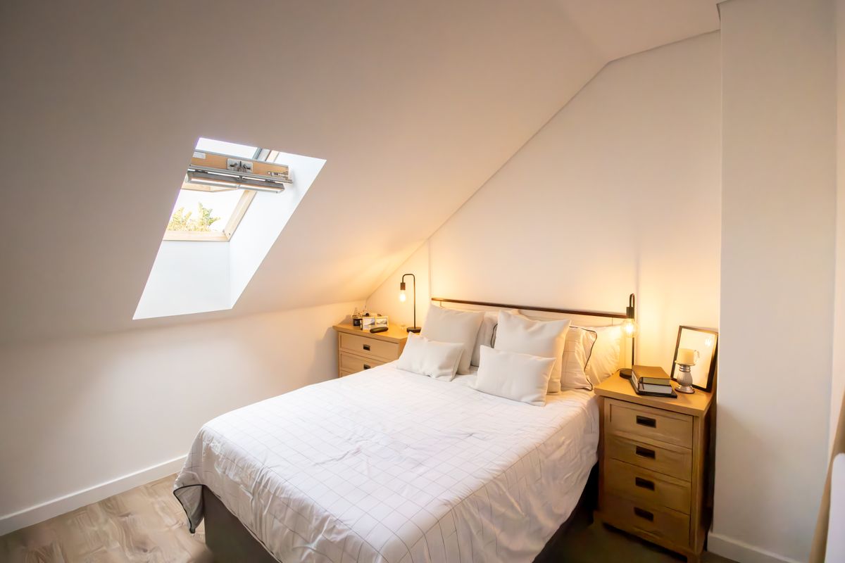 A cozy attic bedroom featuring a sloped ceiling and a functional skylight window, providing natural light and a bright, airy atmosphere.