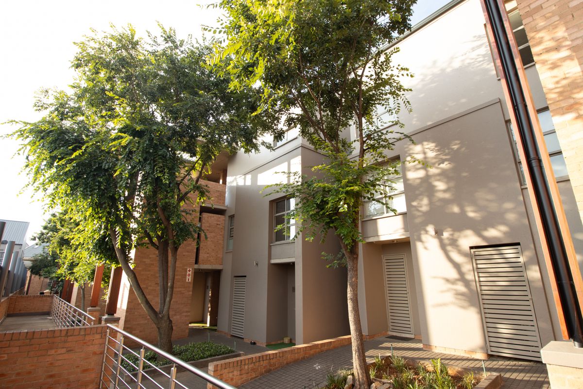 A view of the apartment complex exterior featuring a combination of brick and plastered finishes, paved walkways, and mature trees.