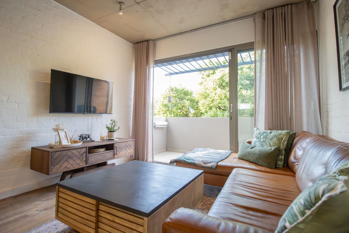 Modern living room featuring an exposed concrete ceiling, painted brick walls, and direct access to a private balcony through large sliding glass doors.