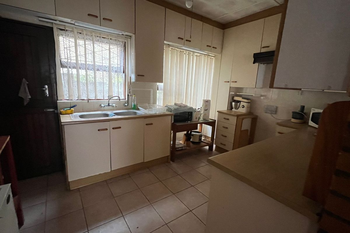 A functional kitchen featuring built-in cabinetry, double basin sink, and tiled flooring, offering potential for modernization and cosmetic updates.
