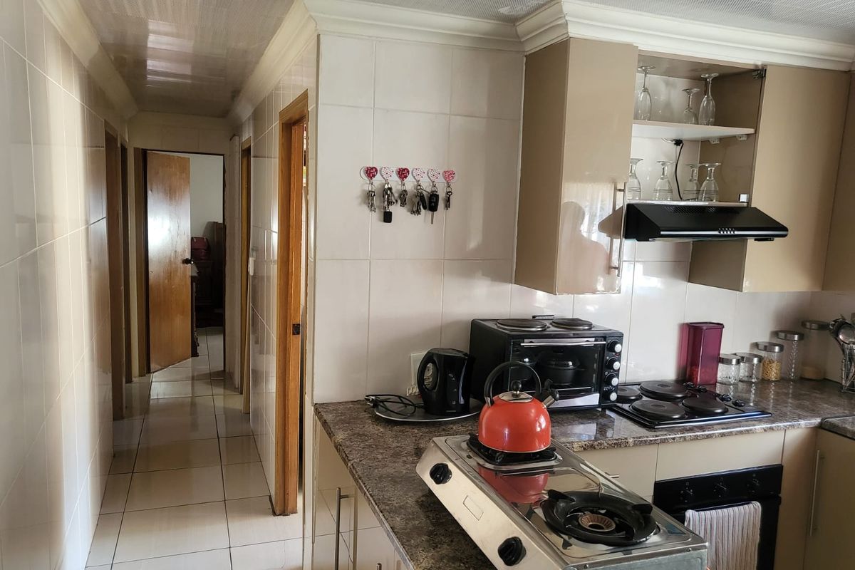 A functional kitchen featuring built-in cabinetry, granite countertops, a built-in oven, and a ceramic hob, with tiled walls and flooring throughout.