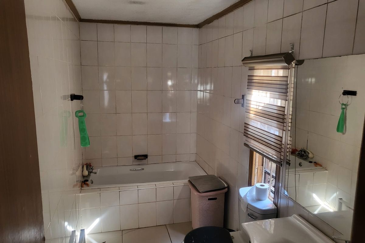 A dated bathroom featuring a built-in bathtub, pedestal sink, and full-height ceramic wall tiling, requiring cosmetic updates to modernize the space.