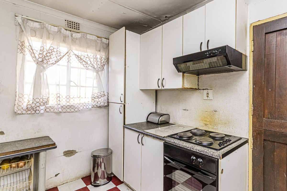 A compact kitchen featuring built-in cabinetry, an electric hob, and an oven, requiring significant cosmetic updates and repairs to wall and ceiling finishes.