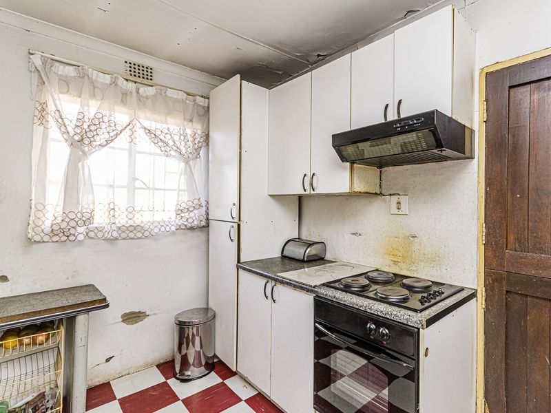 A compact kitchen featuring built-in cabinetry, an electric hob, and an oven, requiring significant cosmetic updates and repairs to wall and ceiling finishes.