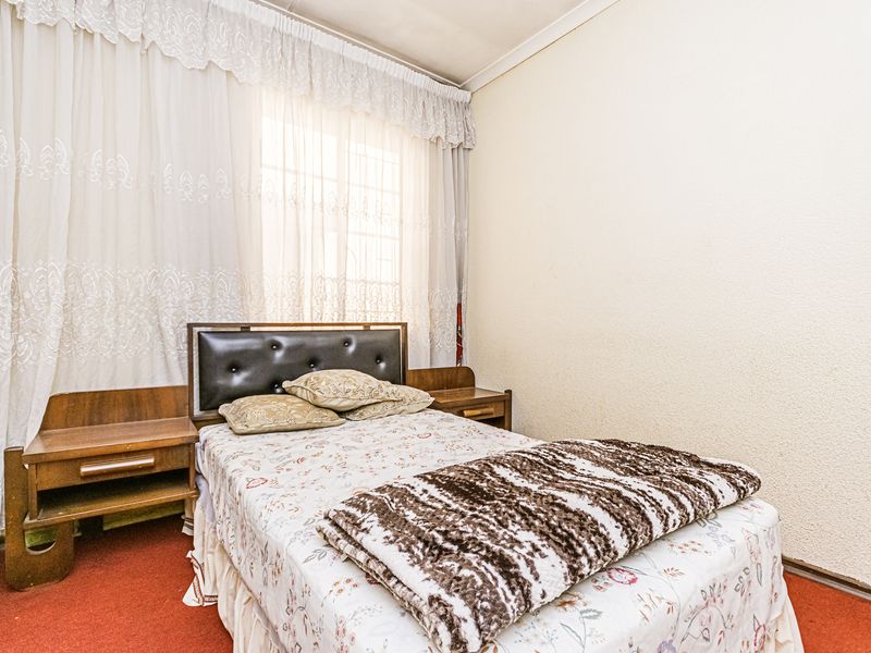 A bedroom featuring built-in bedside cabinetry and a headboard, with red carpeting and window treatments.