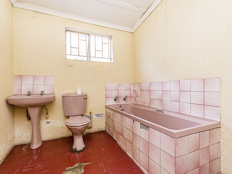 A dated bathroom featuring a pink suite, tiled splashbacks, and damaged flooring, requiring significant renovation and cosmetic updates.
