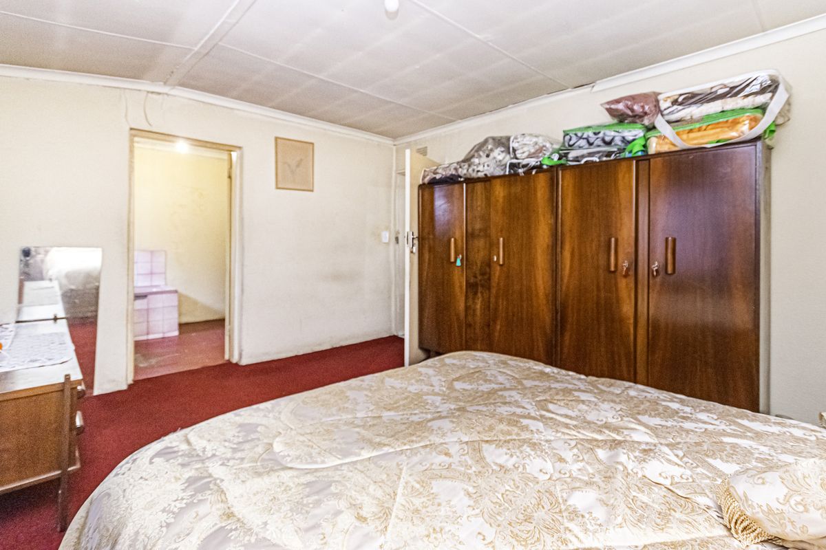 A bedroom featuring built-in wooden wardrobes, carpeted flooring, and a tiled ceiling, with an adjacent room visible through the doorway.