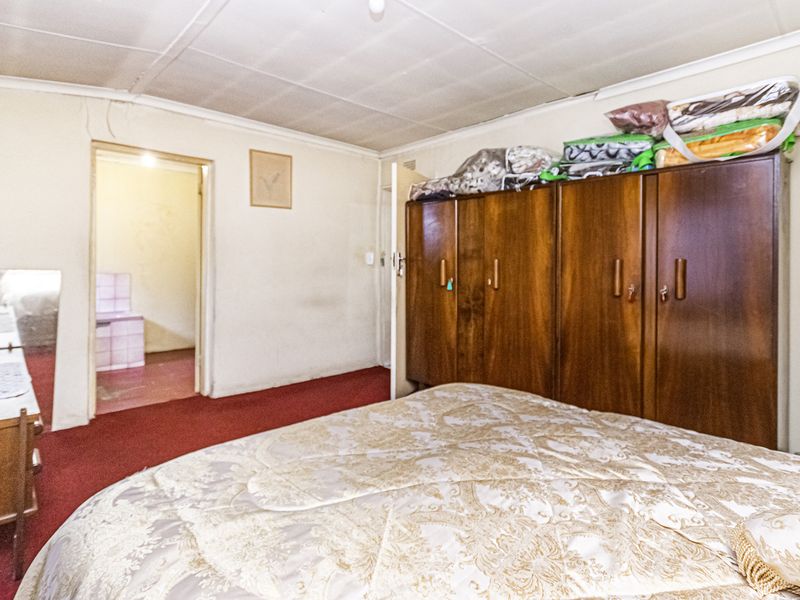 A bedroom featuring built-in wooden wardrobes, carpeted flooring, and a tiled ceiling, with an adjacent room visible through the doorway.
