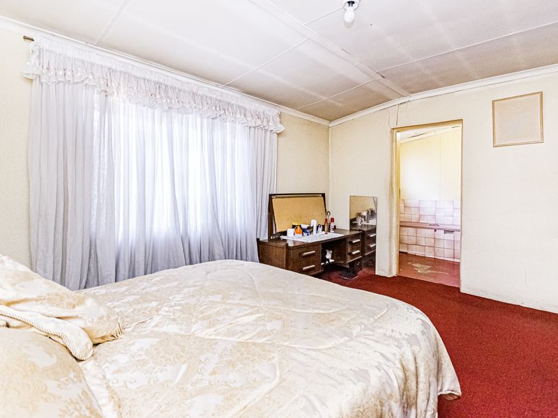 A bedroom featuring red carpet flooring and ceiling tiles, with an adjoining bathroom visible through the doorway.