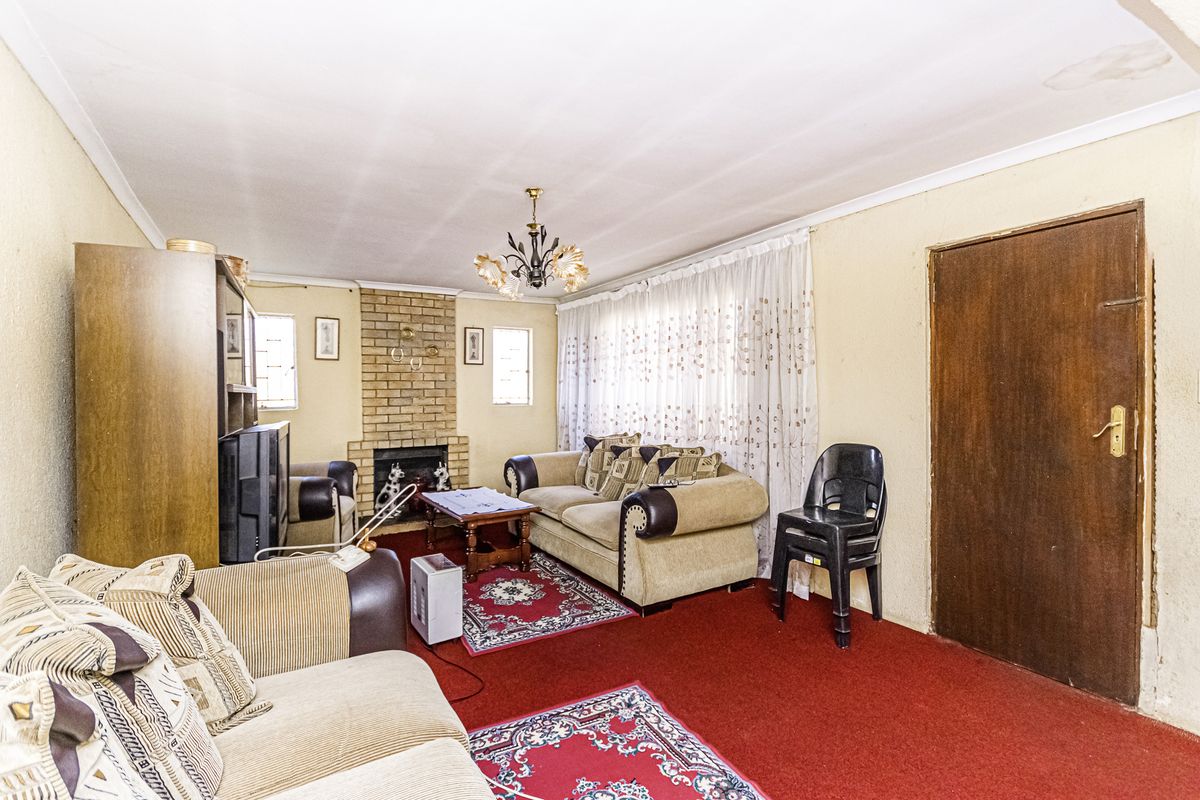 A living room featuring a brick fireplace, cove cornicing, and a timber door, currently finished with dated wall treatments and red carpeting.