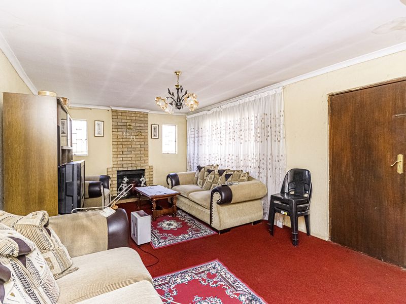 A living room featuring a brick fireplace, cove cornicing, and a timber door, currently finished with dated wall treatments and red carpeting.