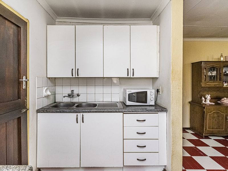 A compact scullery area featuring white built-in cabinetry, a stainless steel sink, and tiled splashback, providing functional utility space.