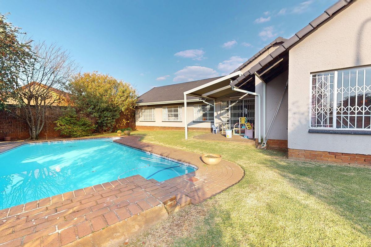 Rear garden featuring a swimming pool with brick coping, a covered patio area, and a well-maintained lawn with perimeter brick boundary walls.