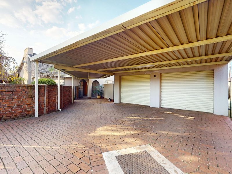 A double garage with metal roller doors and an attached carport, featuring brick paving and a brick boundary wall.