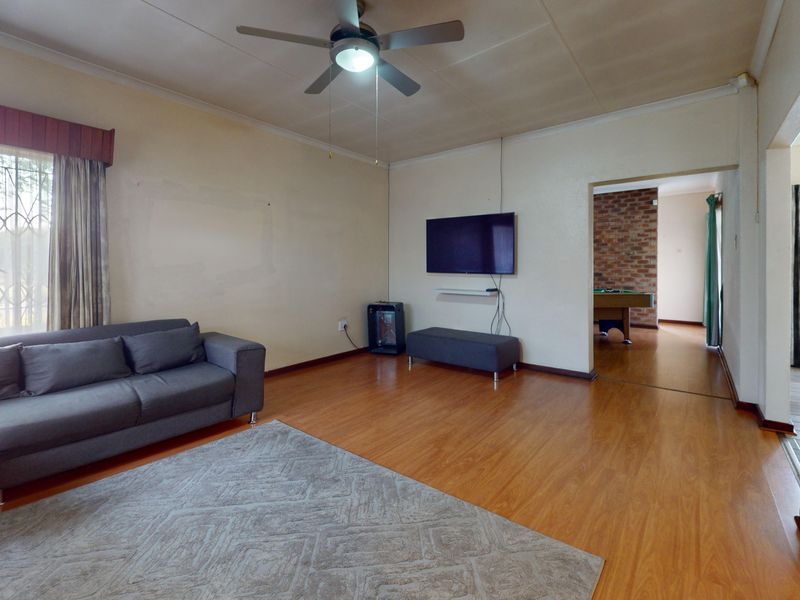 A living room featuring laminate flooring, a ceiling fan, and a security gate, with an adjacent room visible through the doorway.