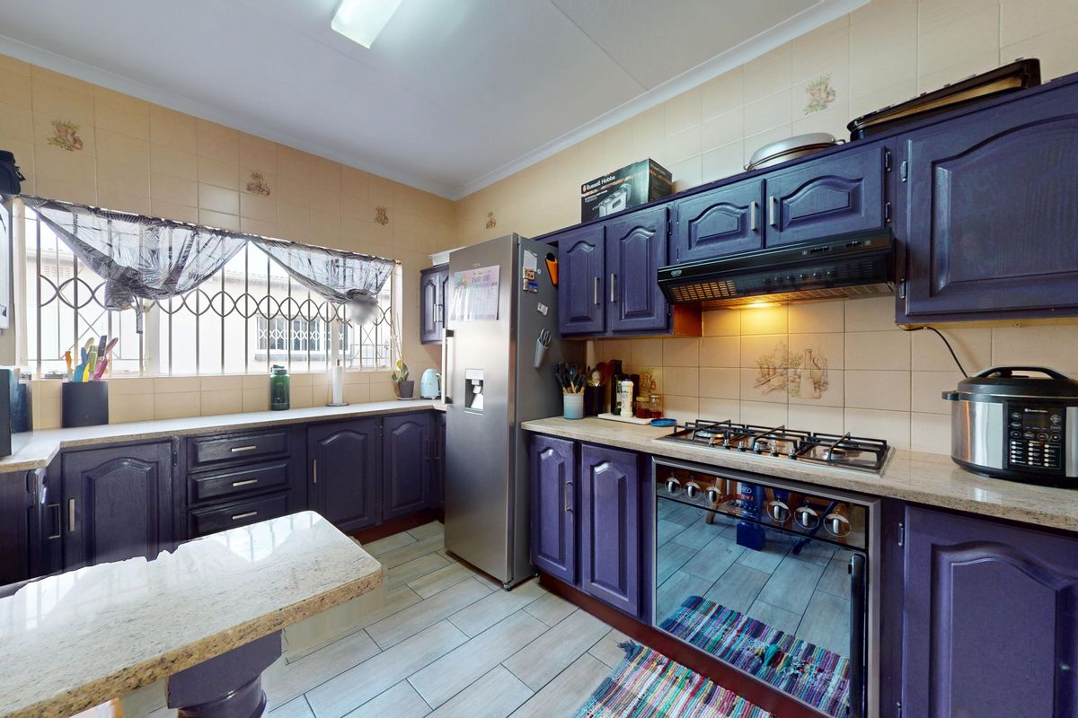 A functional kitchen featuring dark cabinetry, stone countertops, a gas hob with extractor fan, and tiled splashbacks with security bars on the window.