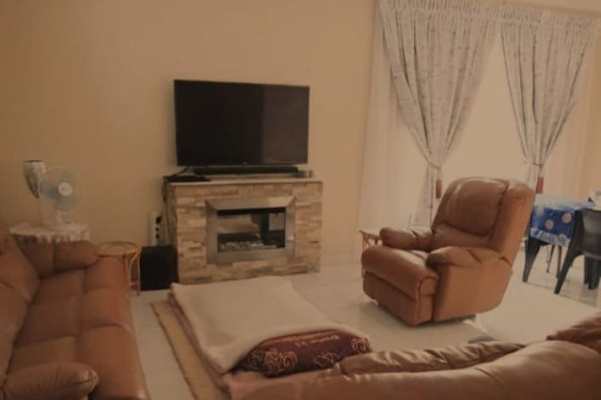 A living room featuring tiled flooring, a stone-clad fireplace, and a ceiling fan, offering a comfortable space for relaxation.