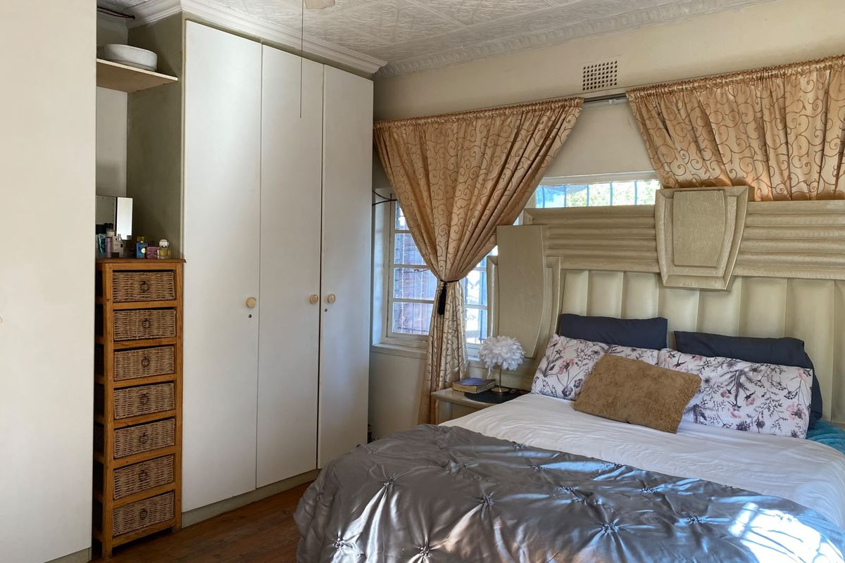 A bedroom featuring built-in cupboards, timber flooring, and a decorative pressed metal ceiling, offering a classic aesthetic with potential for modern updates.