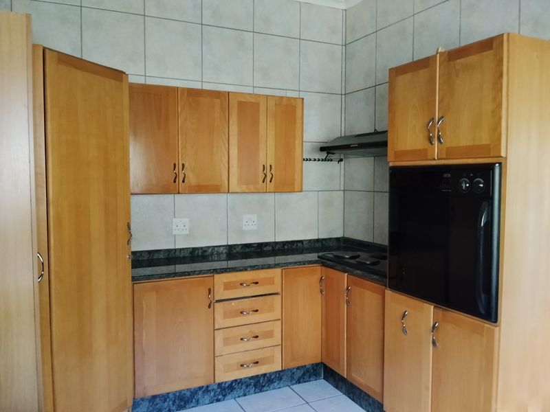 A functional kitchen featuring wooden cabinetry, granite countertops, built-in oven, hob, and extractor fan with neutral tiled splashbacks and flooring.