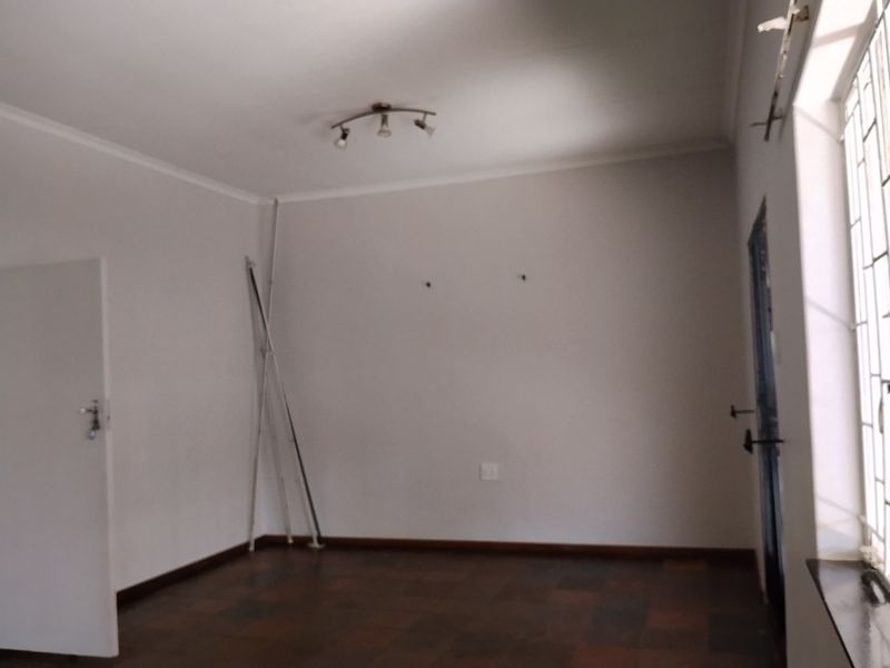An empty living room featuring dark parquet flooring, neutral walls, and security features on the windows and doors.