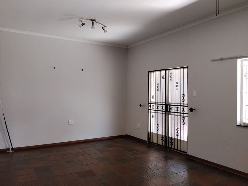 An empty living room featuring dark tiled flooring, a security gate at the entrance, and neutral wall finishes.