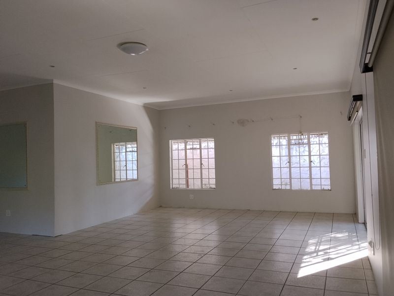 A spacious, empty living area featuring neutral tiled flooring, recessed lighting, and large windows with security bars, providing a blank canvas for interior design.