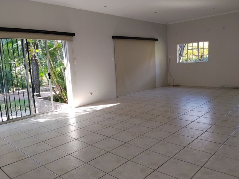 A spacious, empty living area featuring neutral tiled flooring, recessed lighting, and large sliding glass doors providing direct access to the garden.