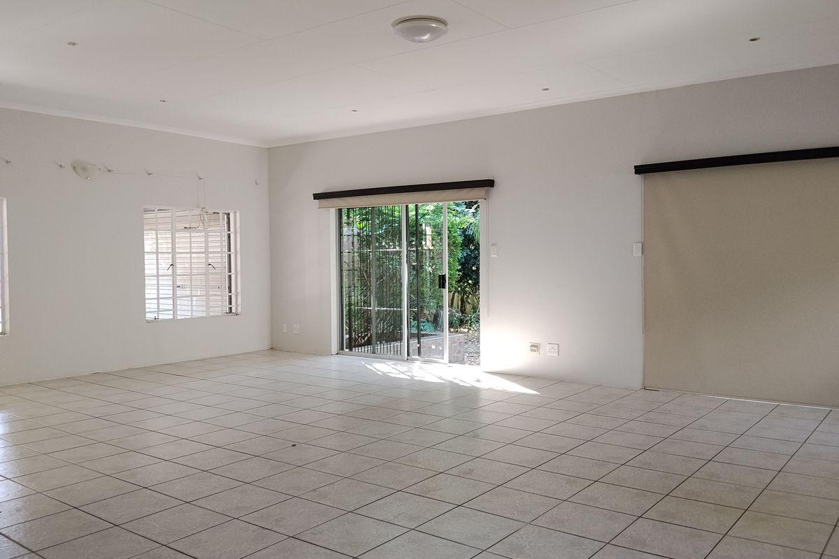 A spacious, empty living area featuring neutral tiled flooring, recessed lighting, and a sliding glass door providing access to the garden.