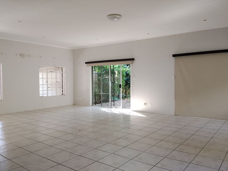 A spacious, empty living area featuring neutral tiled flooring, recessed lighting, and a sliding glass door providing access to the garden.