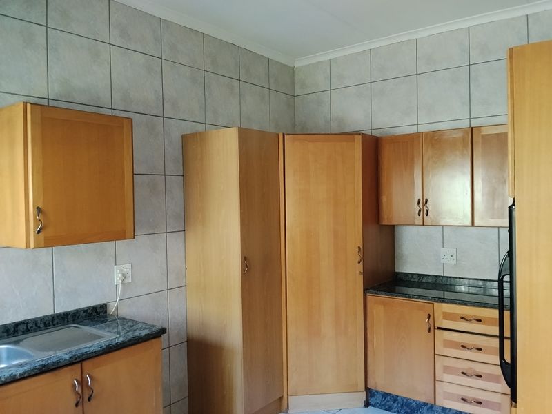 A functional kitchen featuring wood-finish cabinetry, granite countertops, and full-height wall tiling, offering ample storage space.