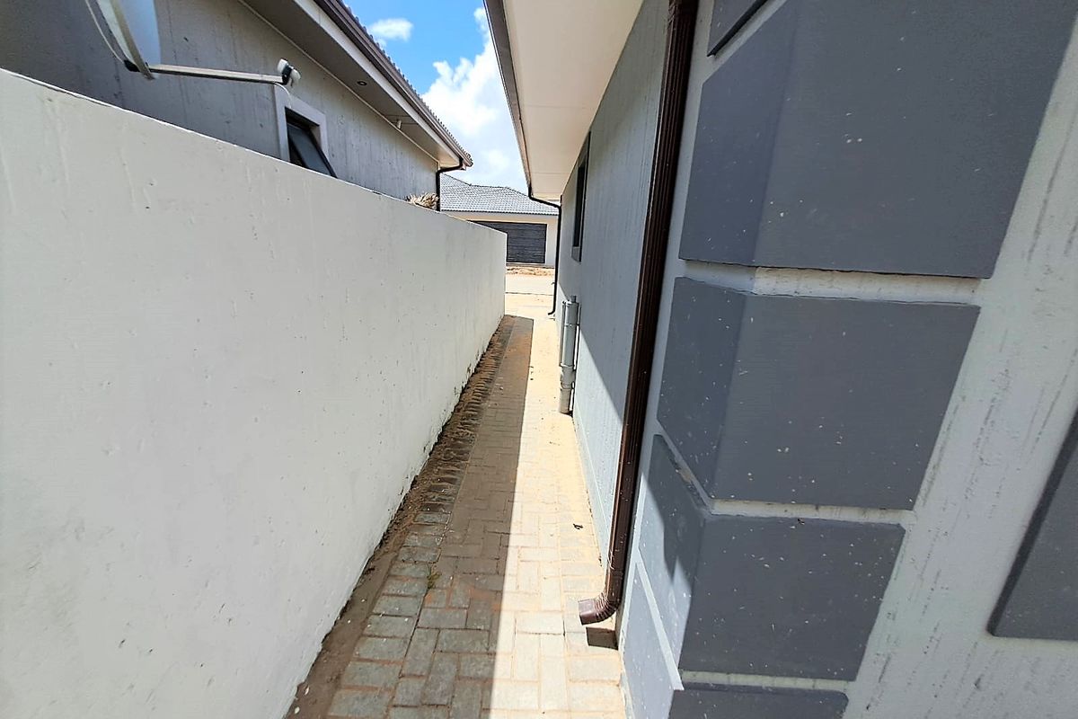 A narrow paved side passage between the cluster home and the boundary wall, featuring functional drainage downpipes and clean exterior finishes.