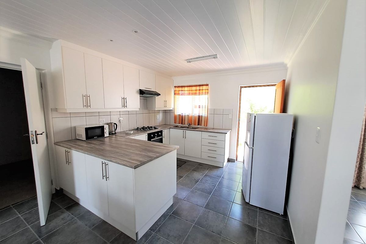 A functional kitchen featuring white cabinetry, wood-look laminate countertops, a gas hob, built-in oven, and tiled flooring with direct access to the exterior.