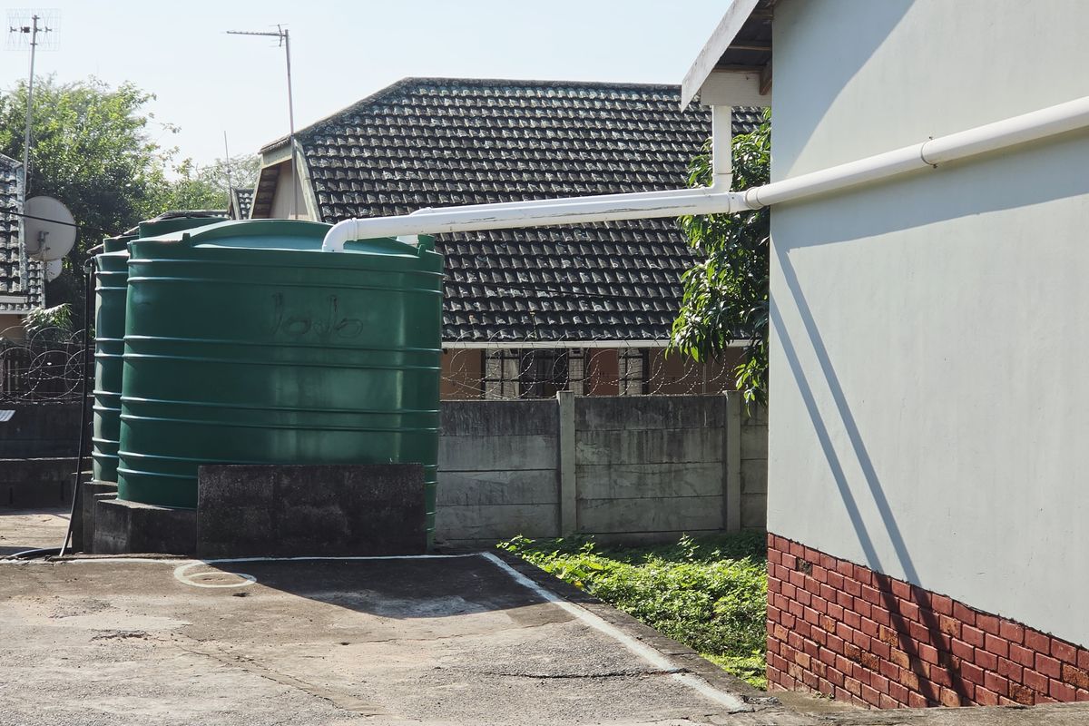 Rear exterior area featuring large green water storage tanks connected to the building's guttering system, set against a concrete boundary wall.
