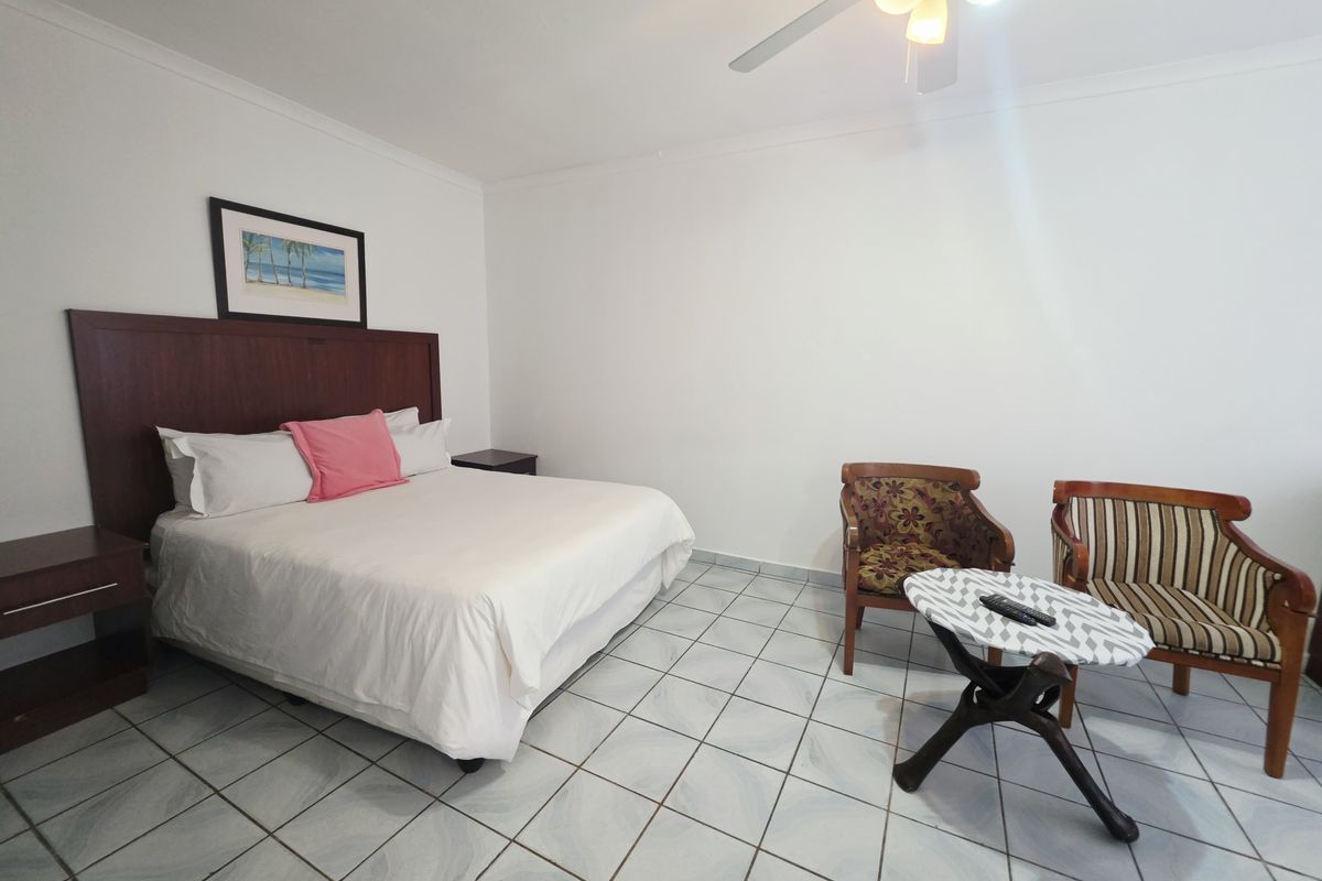 A spacious bedroom featuring tiled flooring, a ceiling fan, and neutral wall finishes, providing a clean and functional sleeping area.