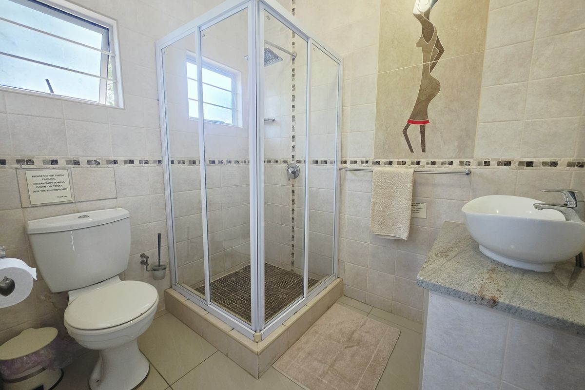 A functional bathroom featuring a glass-enclosed shower, a vanity basin with a granite countertop, and neutral wall tiling with decorative accents.