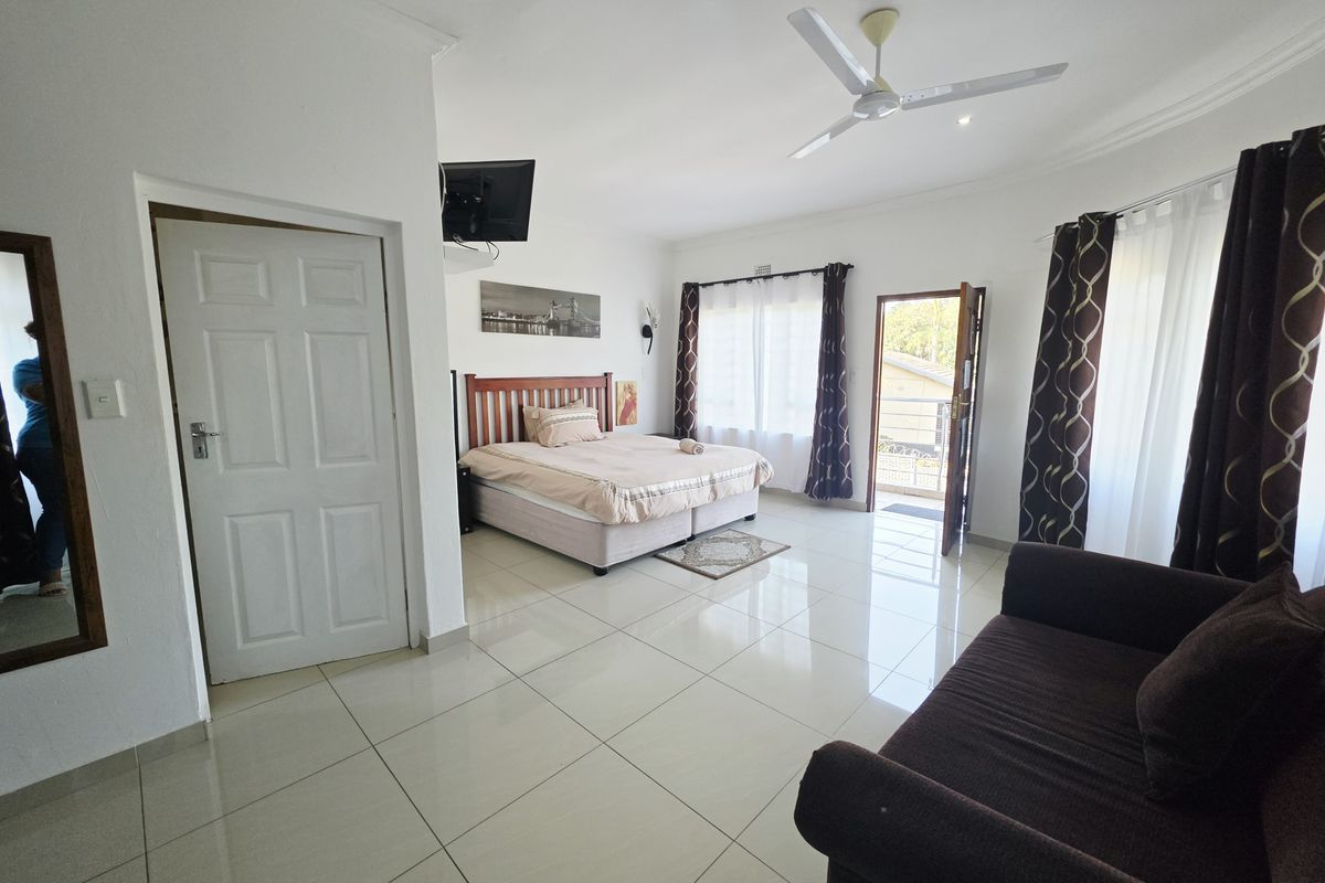 A spacious bedroom featuring tiled flooring, a ceiling fan, and direct access to an outdoor area through a private door.