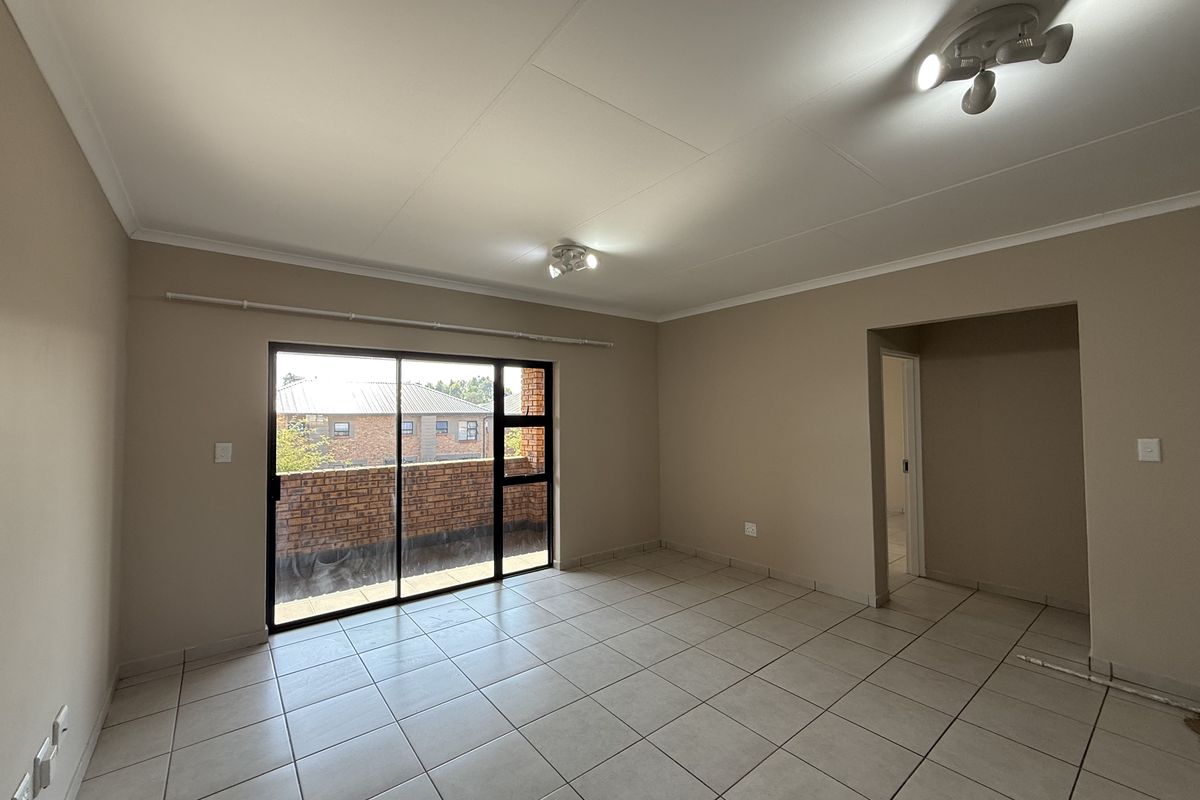 A spacious, empty living room featuring neutral tiled flooring, coved ceilings, and a large sliding glass door providing access to an outdoor balcony area.