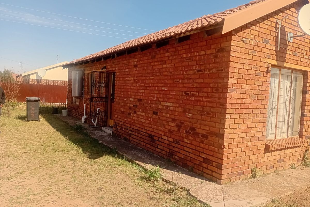 Rear view of a single-story face-brick house featuring a tiled roof, security gate, and external electric geyser unit.